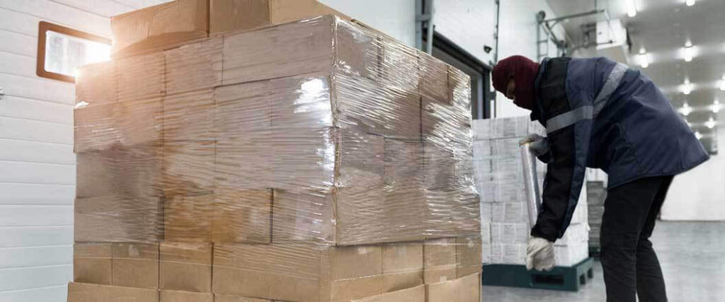 refrigerated warehouse worker shrink-wrapping boxes on a pallet. 