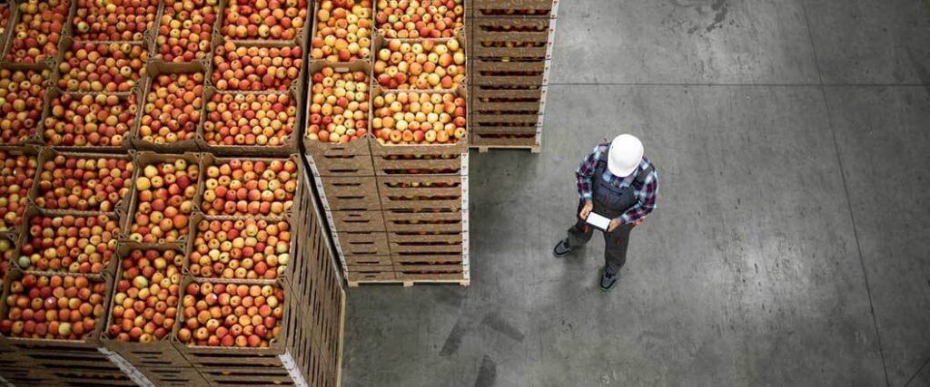 An overhead view of a warehouse worker taking inventory of stacked crates of apples