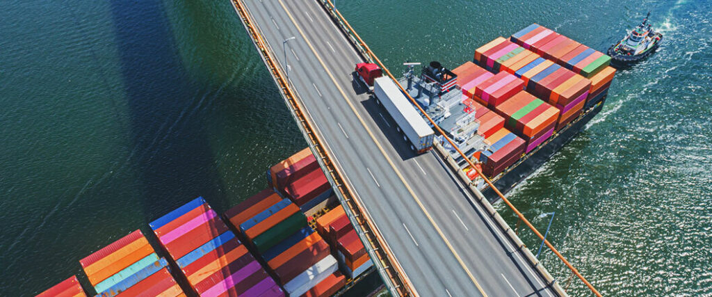 A semi truck on a bridge with a cargo vessel passing under the bridge, showing part of the process of how to ship seafood